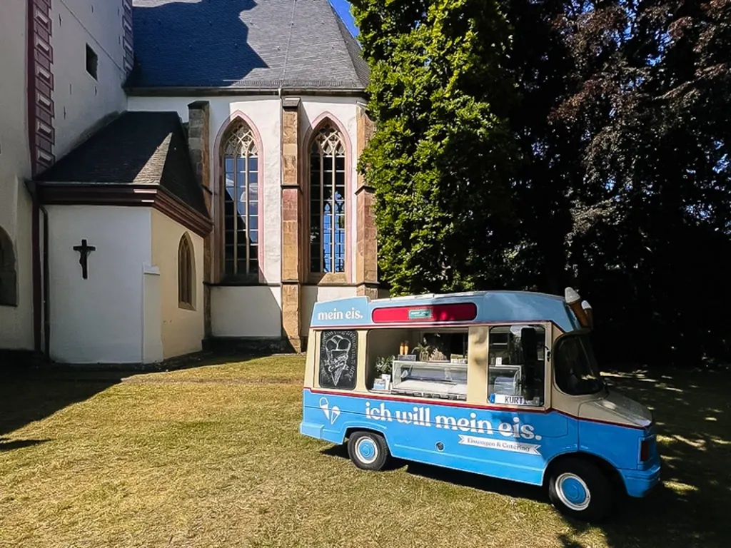 Oldtimer-Eiswagen Kurti von mein eis auf einer sonnigen Wiese neben einer alten Kirche